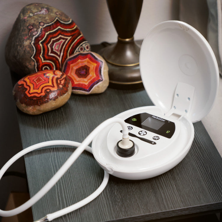 Herbalizer with a power cord on a dark surface, surrounded by decorative stones.